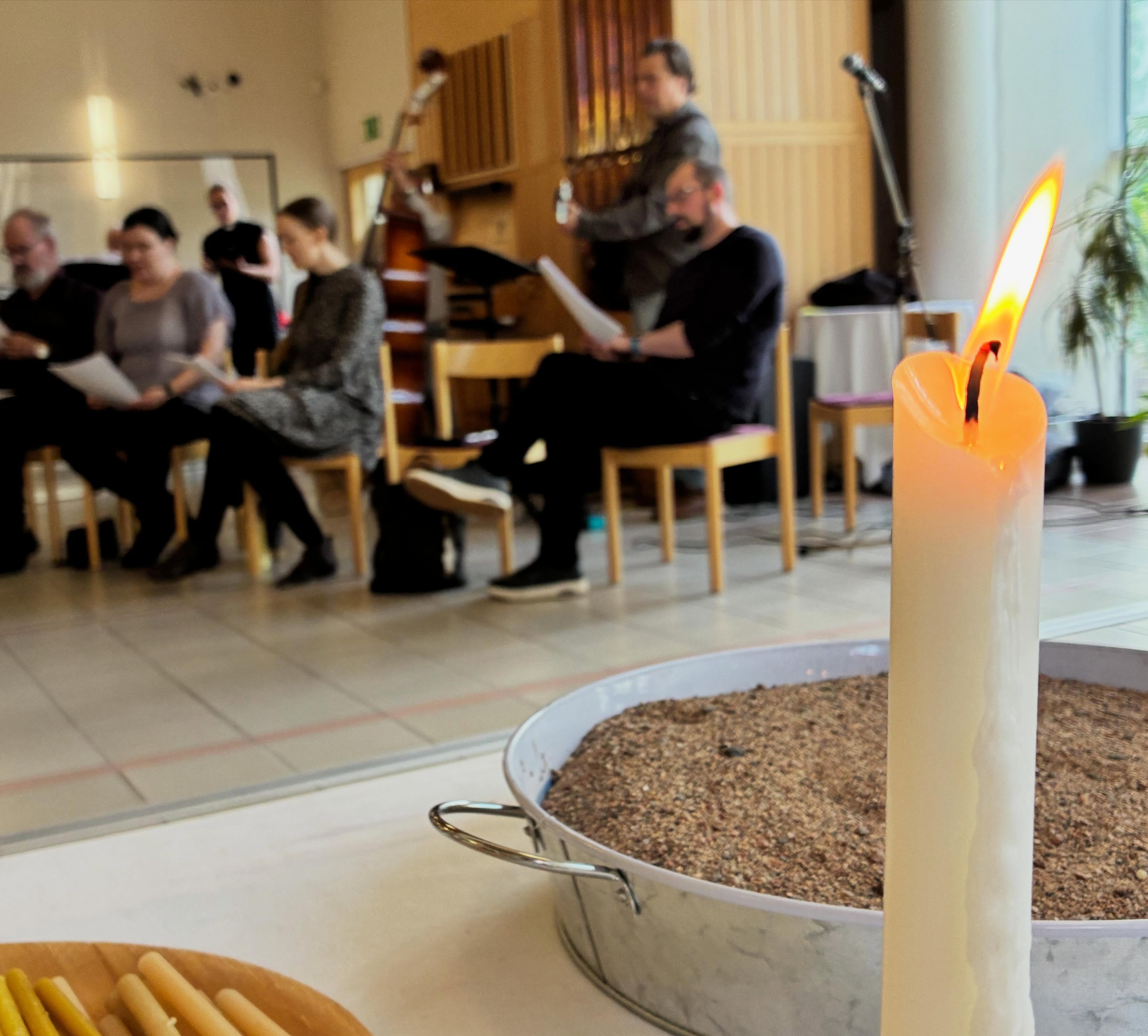 Ljus och skål med sand, personer sjunger i kyrksal.