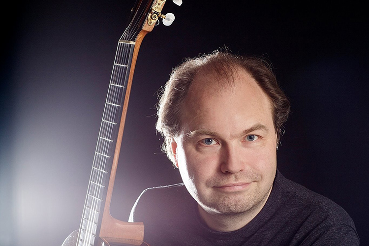 Osmo Palmu på gitarr framför spansk-finsk musik Osmo Palmu med gitarr i famnen. Endast en del av gitarren syns.