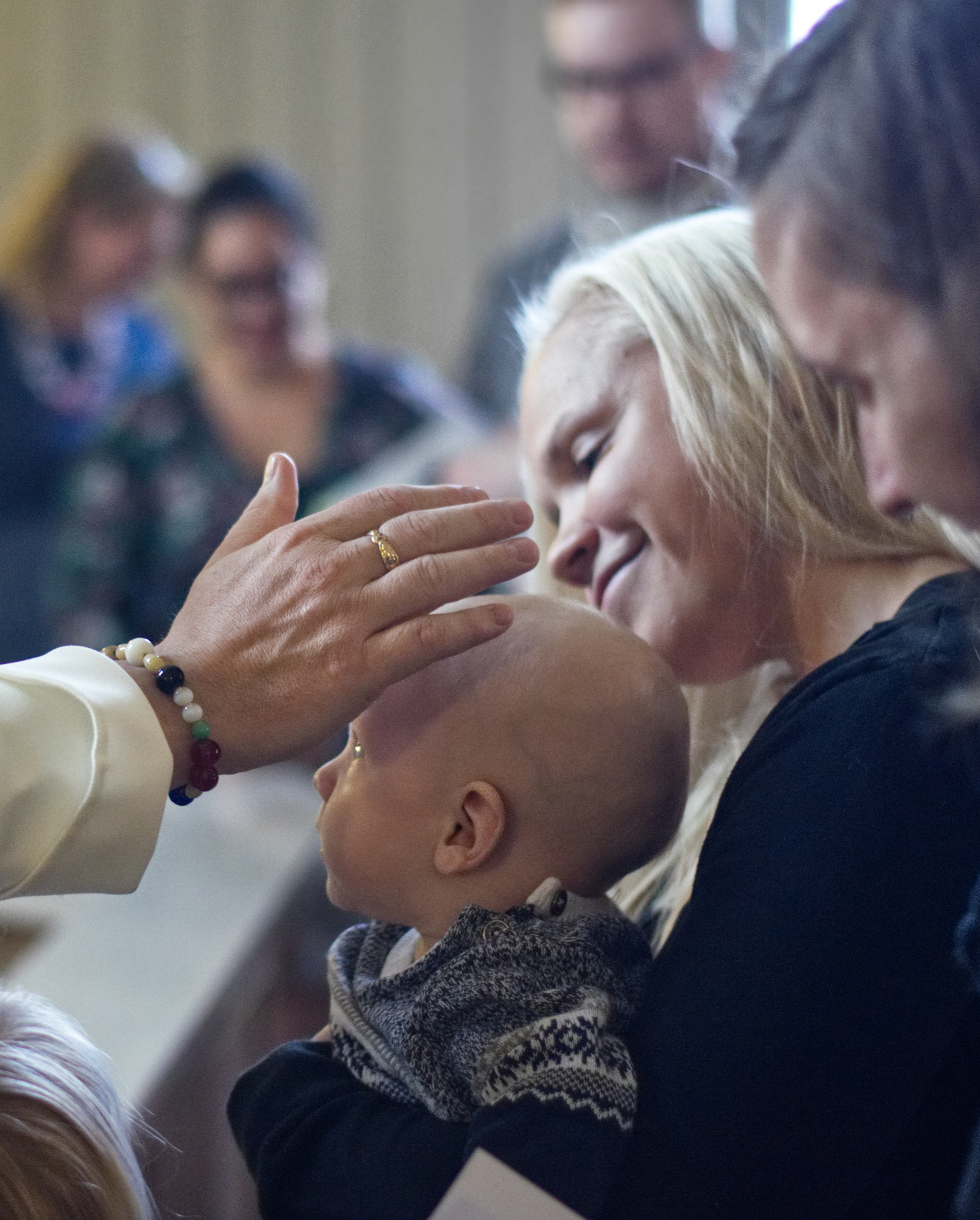Babykyrka baby som prästen välsignar i sin mammas famn