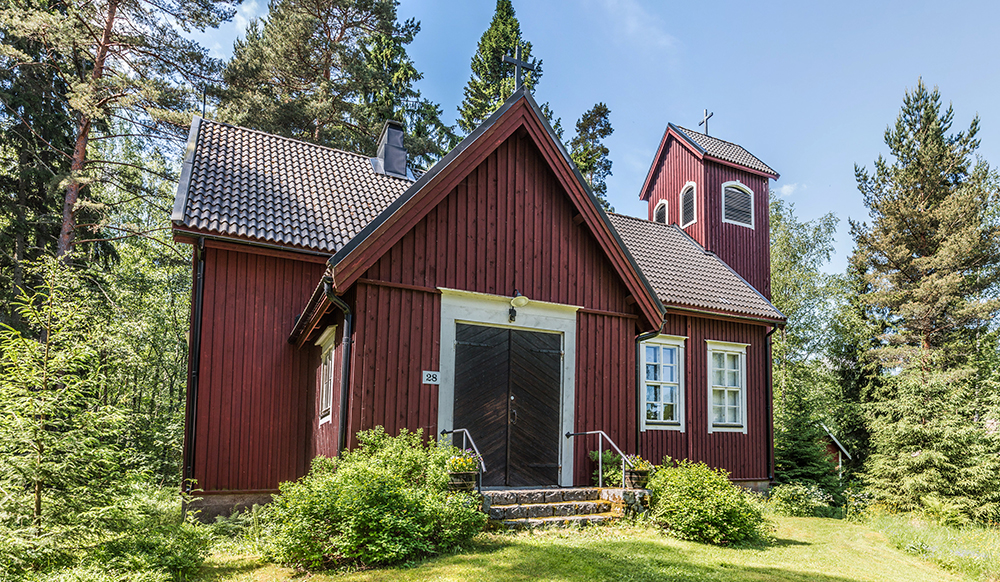 Röd träkyrka på landet i grönskan.
