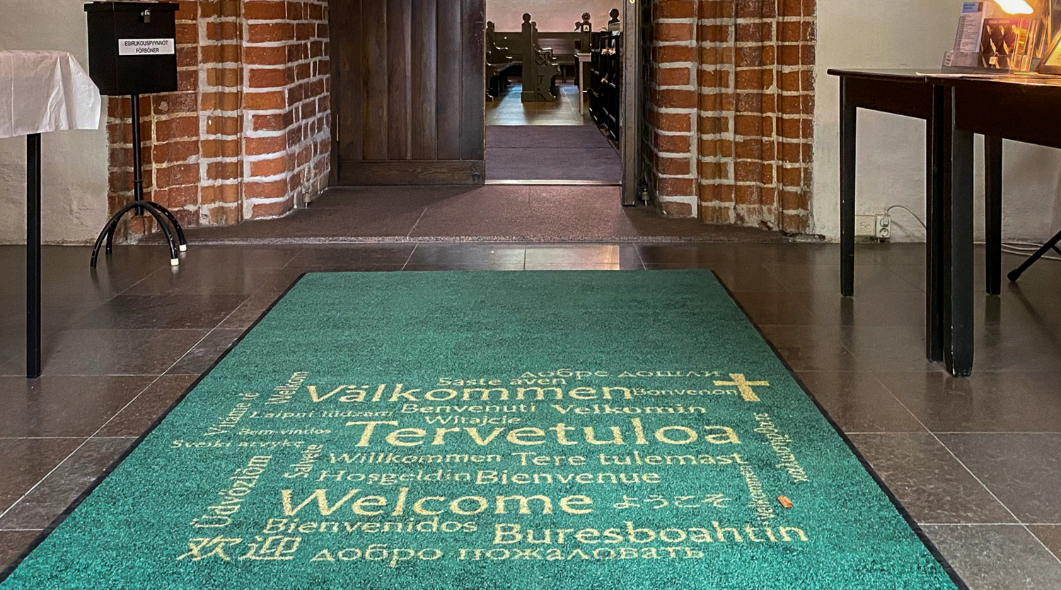 Matta med texten Välkommen på olika språk i tamburen till domkyrkan.