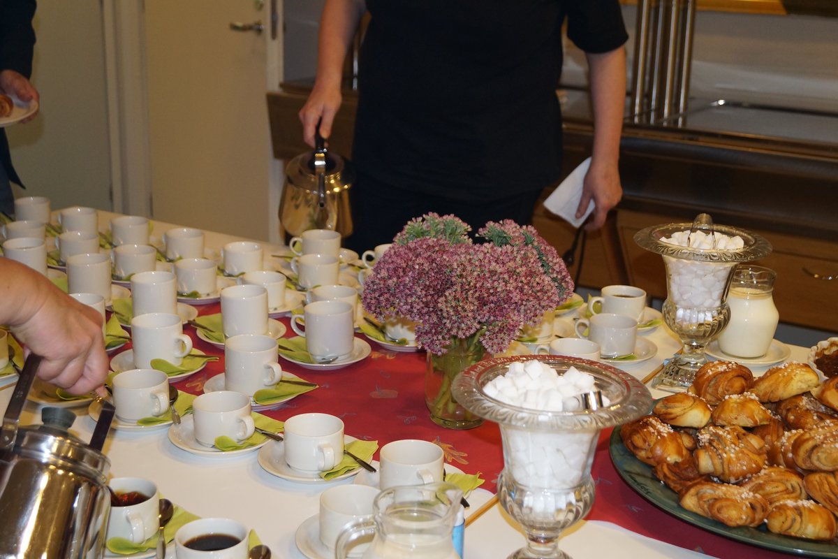 Husmor häller i kaffe i kopparna på ett dukat bord.